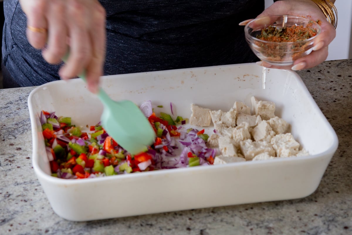 stirring spices into the veggies in the baking pan