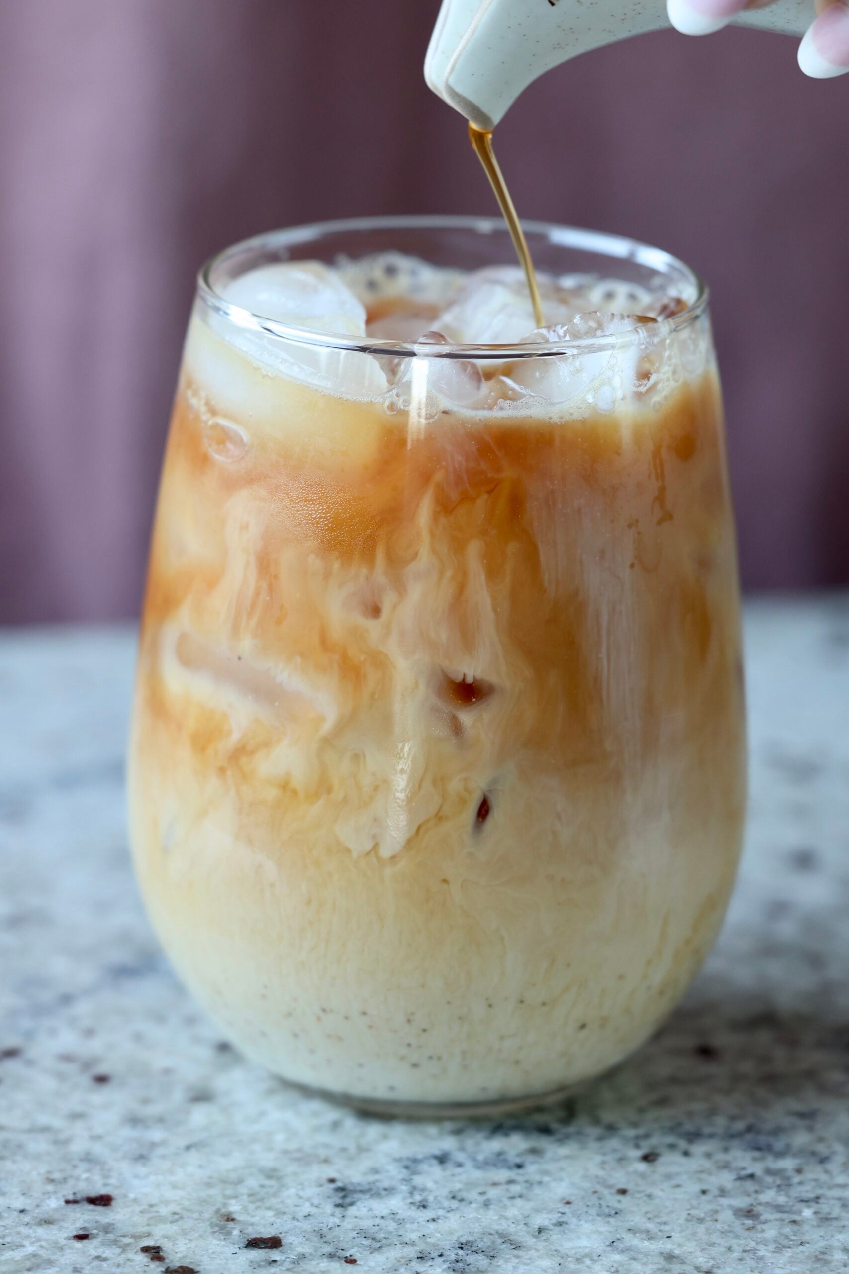 pouring chai concentrate into a glass of iced chai