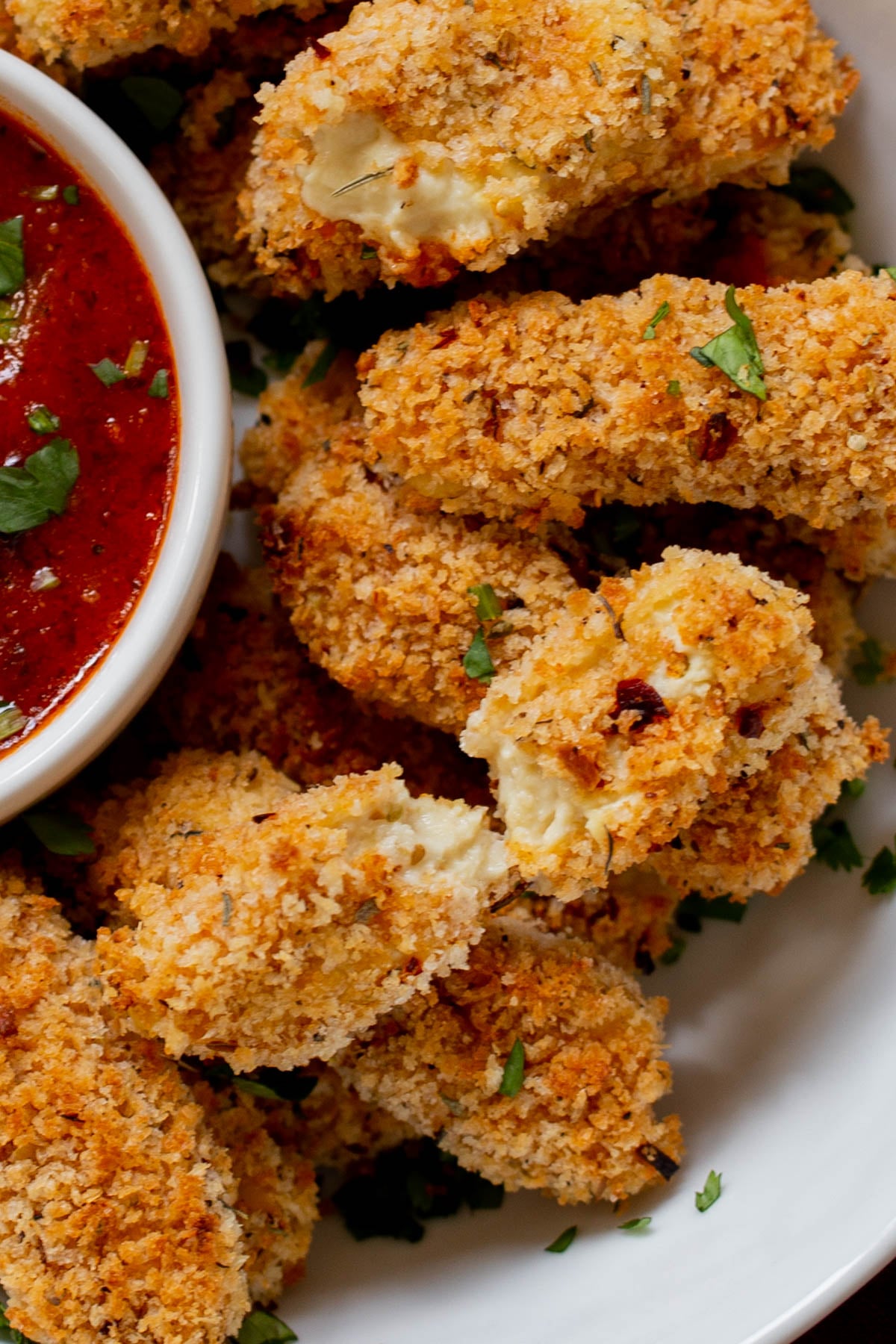 extreme close-up of vegan mozzarella sticks in a serving platter with marinara on the side with some broken sticks, so you can see the cheese