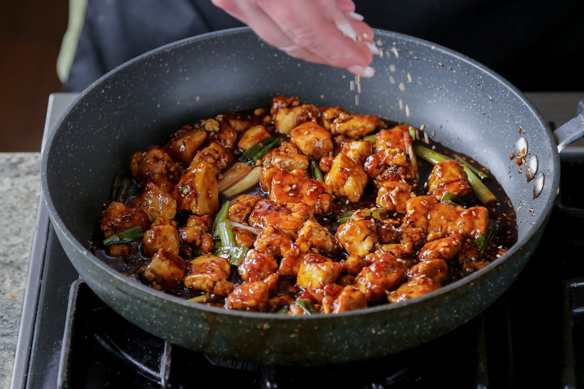 topping the teriyaki tofu in the pan with sesame seeds