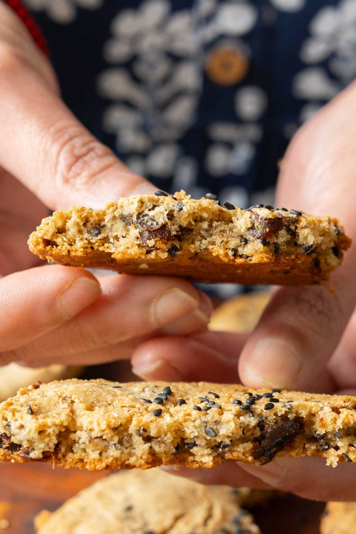 close-up of hands holding a broken black sesame cookie so you can see the texture and dates inside