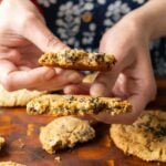hands holding a broken black sesame cookie so you can see the texture and dates inside