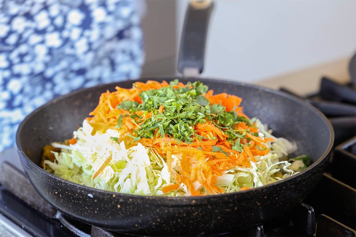 adding cabbage, carrots, and cilantro to the pan