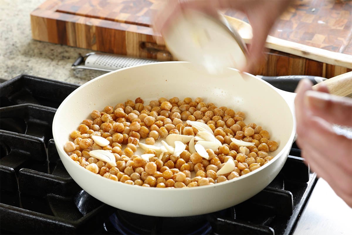 adding garlic to the pan of chickpeas