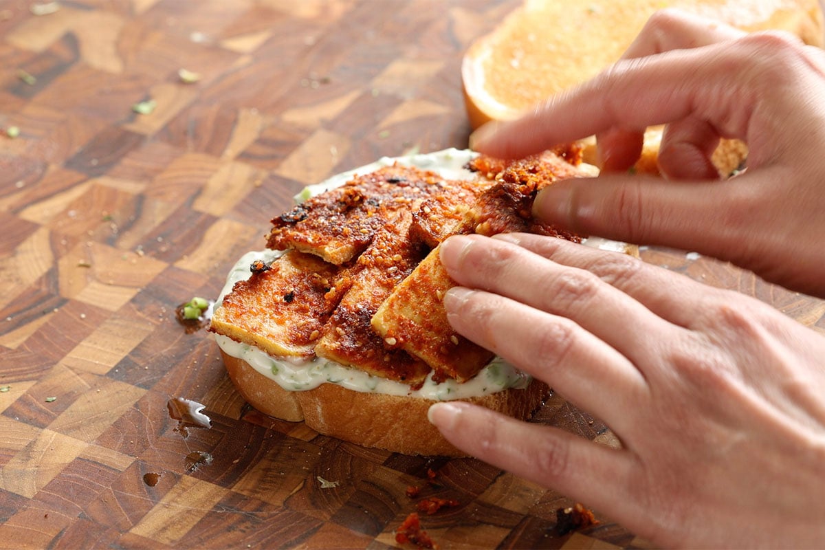 adding the yogurt sauce and coconut tofu to the sandwich