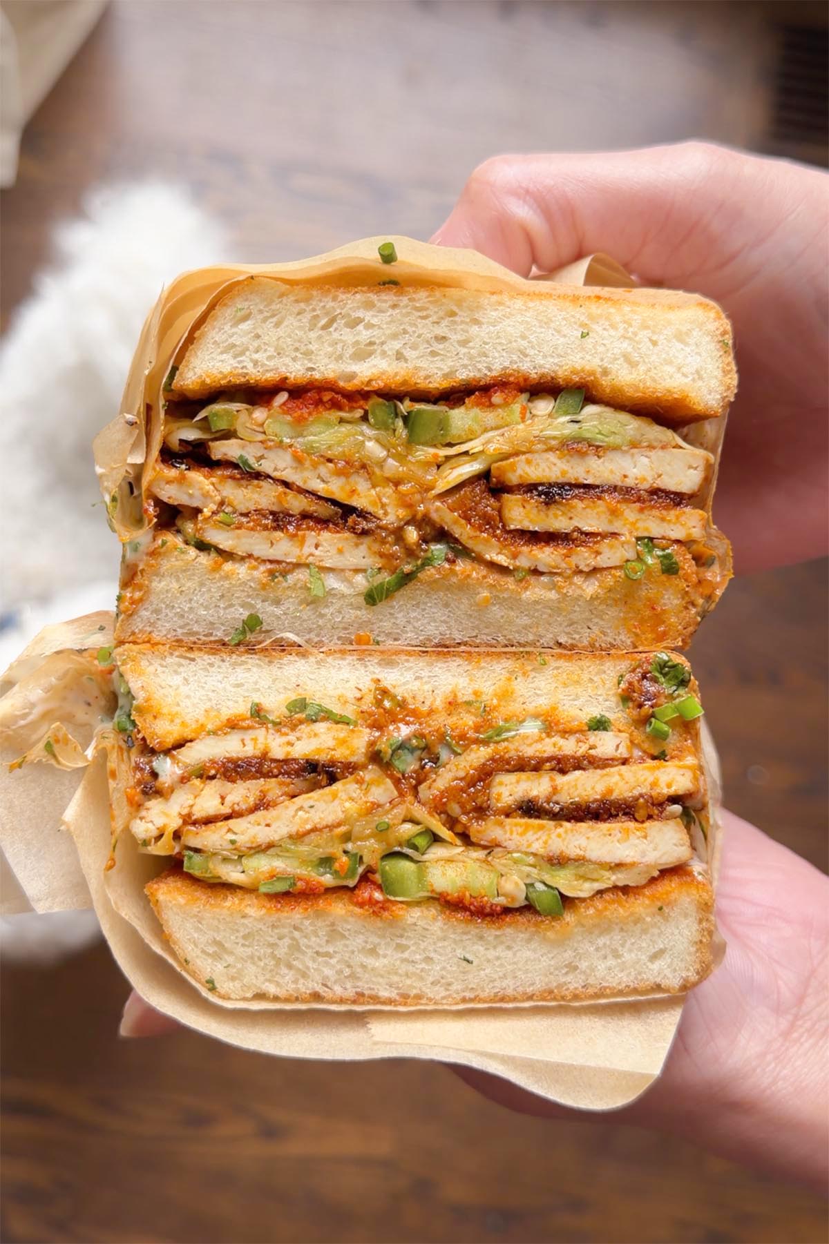 hand holding a coconut tofu sandwich wrapped in butcher paper