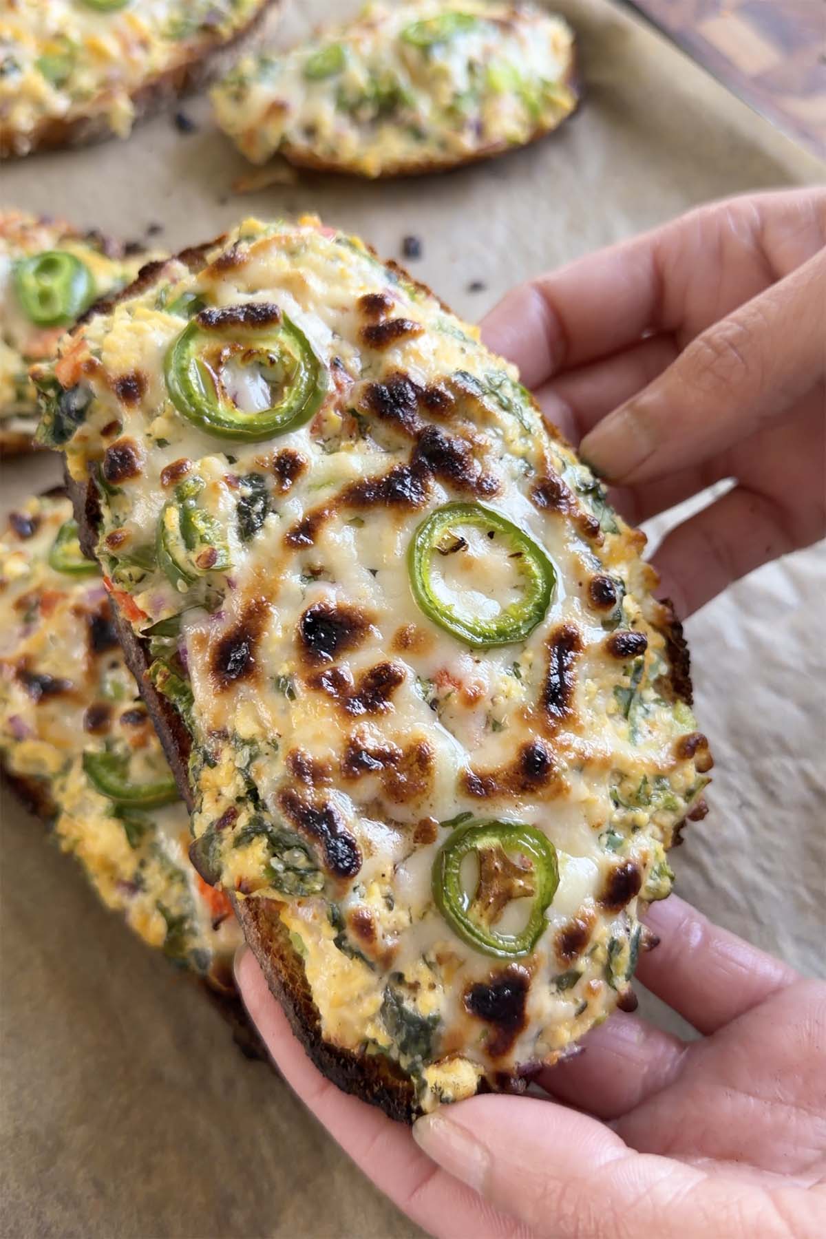 hands holding a slice of chilli cheese toast before topping