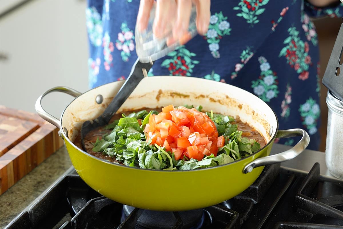 adding kale and tomato to the pan