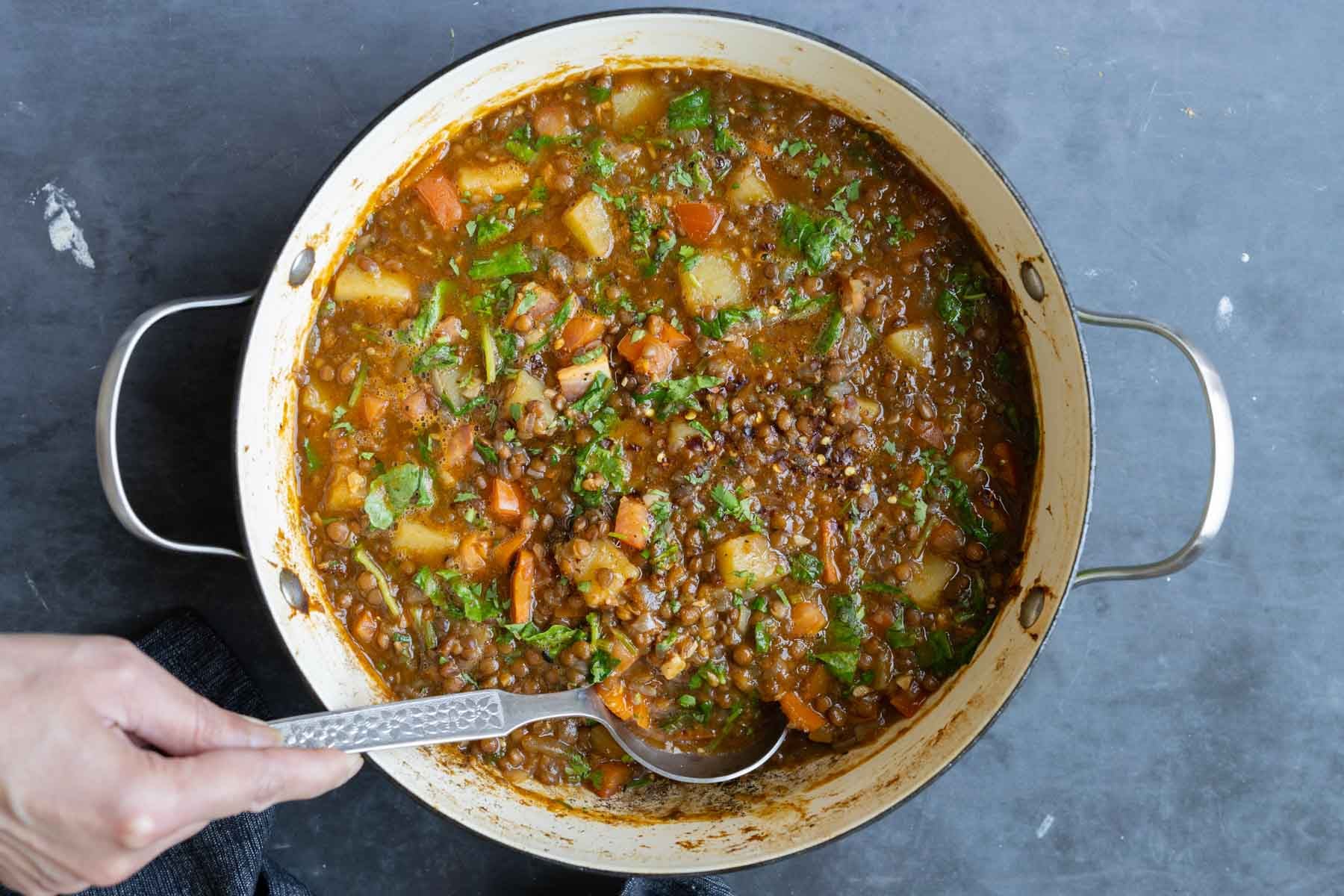 spoon serving some lentil potato soup from the pot